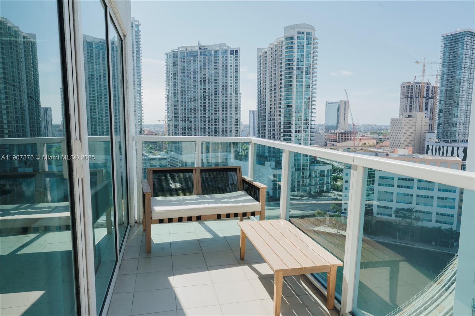 A balcony with a wooden bench and table overlooks a city skyline with skyscrapers — 41 SE 5th St # 1217, Miami FL 33131, MIAMI, FL