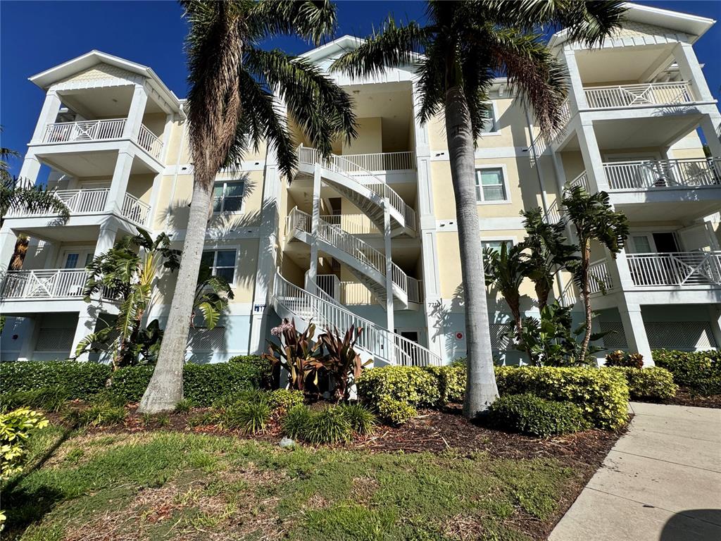 A multi-story apartment building features white balconies, exterior staircases, and palm trees in front — 7710 34TH AVENUE W UNIT 202, BRADENTON, FL