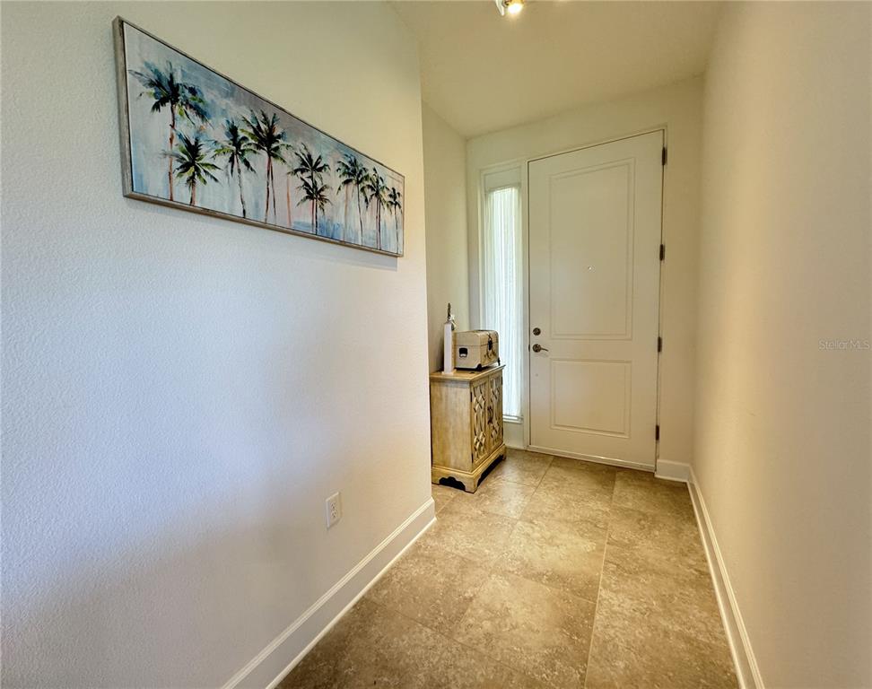 An entryway features tile flooring, a white front door, and a palm tree wall painting — 7710 34TH AVENUE W UNIT 202, BRADENTON, FL