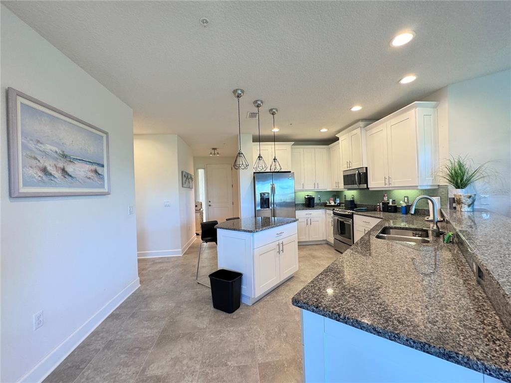 A kitchen features white cabinets, granite countertops, a center island, and stainless steel appliances — 7710 34TH AVENUE W UNIT 202, BRADENTON, FL