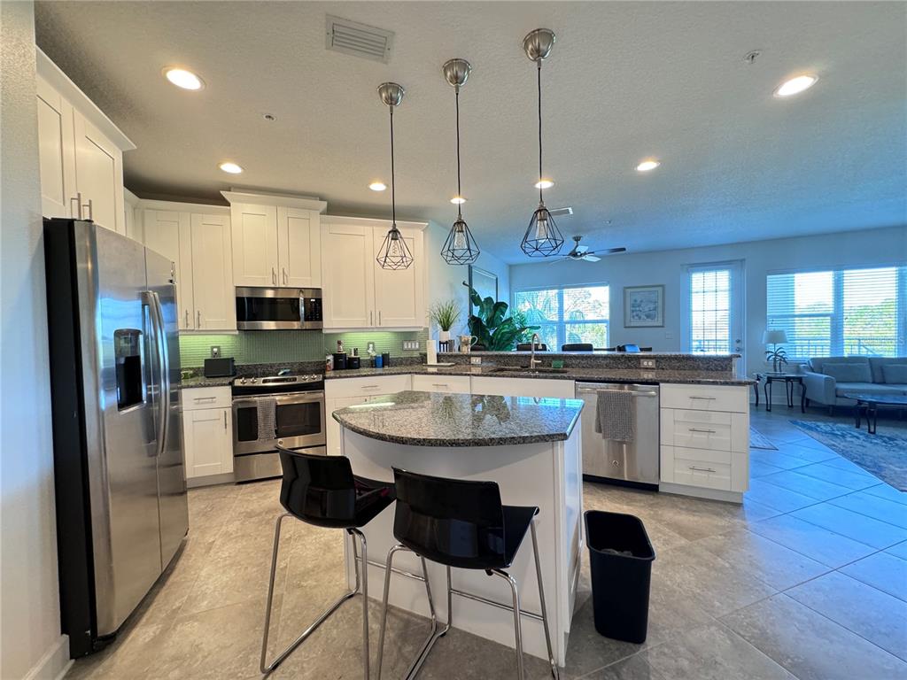 A kitchen features white cabinetry, granite countertops, stainless steel appliances, and a central island — 7710 34TH AVENUE W UNIT 202, BRADENTON, FL
