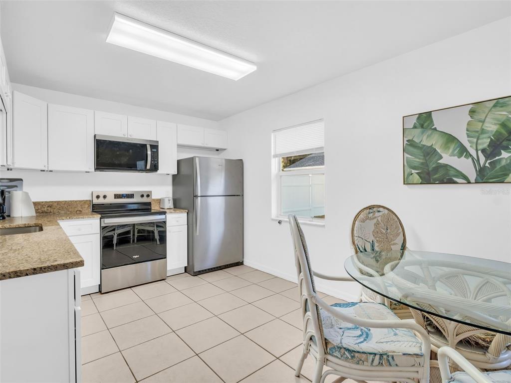A kitchen features white cabinets, stainless steel appliances, granite countertops, and a glass dining table — 103 E PARK STREET, TARPON SPRINGS, FL