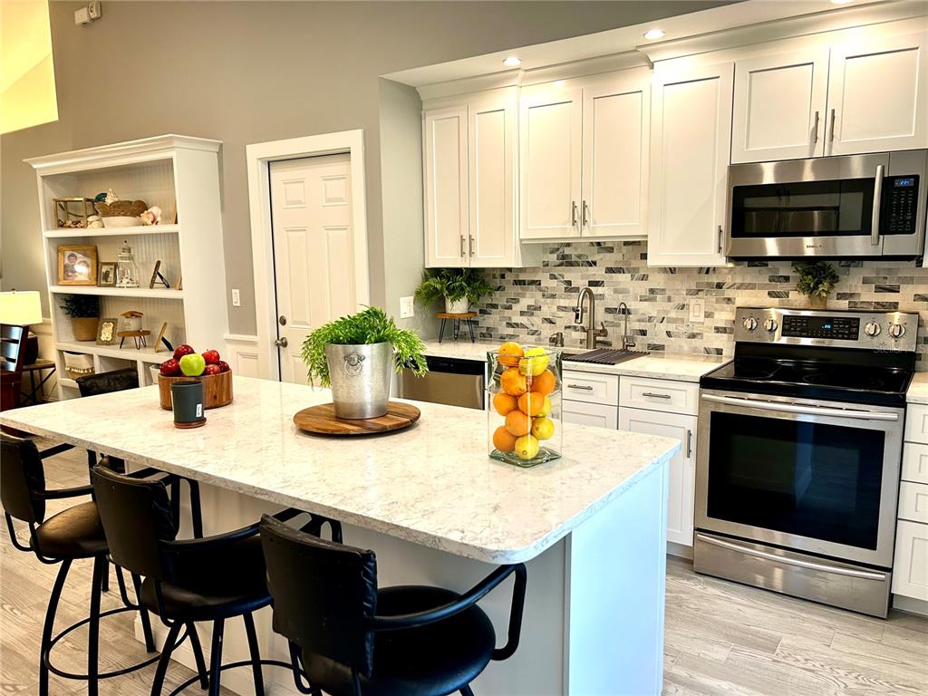 A modern kitchen features white cabinets, a marble-topped island with bar stools, and stainless appliances — 35 RIVERSIDE LANE, PALM COAST, FL