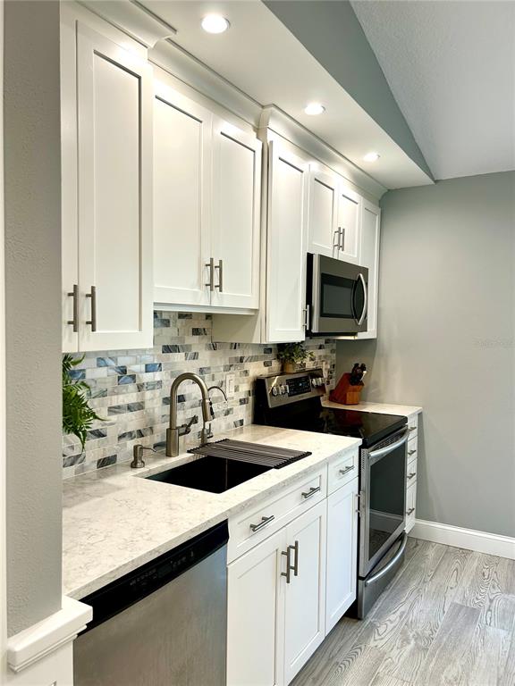 A kitchen features white cabinets, a mosaic tile backsplash, stainless steel appliances, and quartz countertops — 35 RIVERSIDE LANE, PALM COAST, FL
