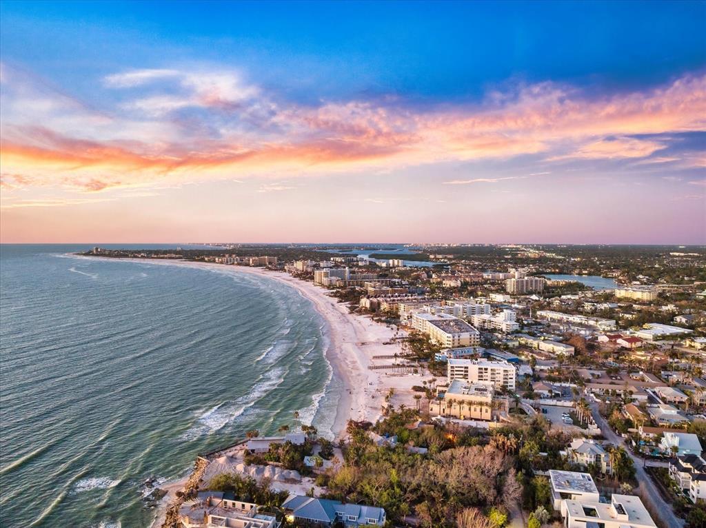 An aerial view shows a sandy beach coastline with buildings and trees at sunset — 116 VISTA HERMOSA CIRCLE UNIT 204C, SARASOTA, FL