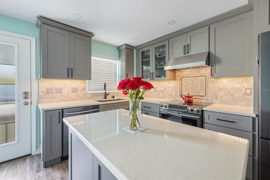 A modern kitchen features gray cabinets, white quartz countertops, a central island, and stainless appliances — 116 VISTA HERMOSA CIRCLE UNIT 204C, SARASOTA, FL