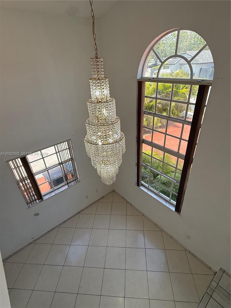 A high-ceilinged room features a large crystal chandelier, tiled floors, and two arched windows — 9940 SW 146th Ct, Miami FL 33186, MIAMI, FL