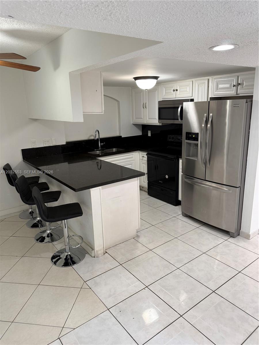 A kitchen features white cabinets, black countertops, stainless steel appliances, and a breakfast bar — 9940 SW 146th Ct, Miami FL 33186, MIAMI, FL
