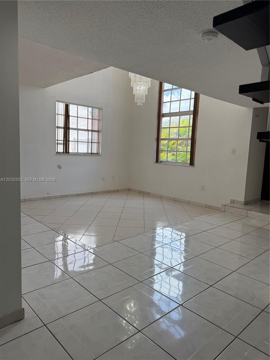 A bright living room features white tiled floors, a crystal chandelier, and large windows — 9940 SW 146th Ct, Miami FL 33186, MIAMI, FL