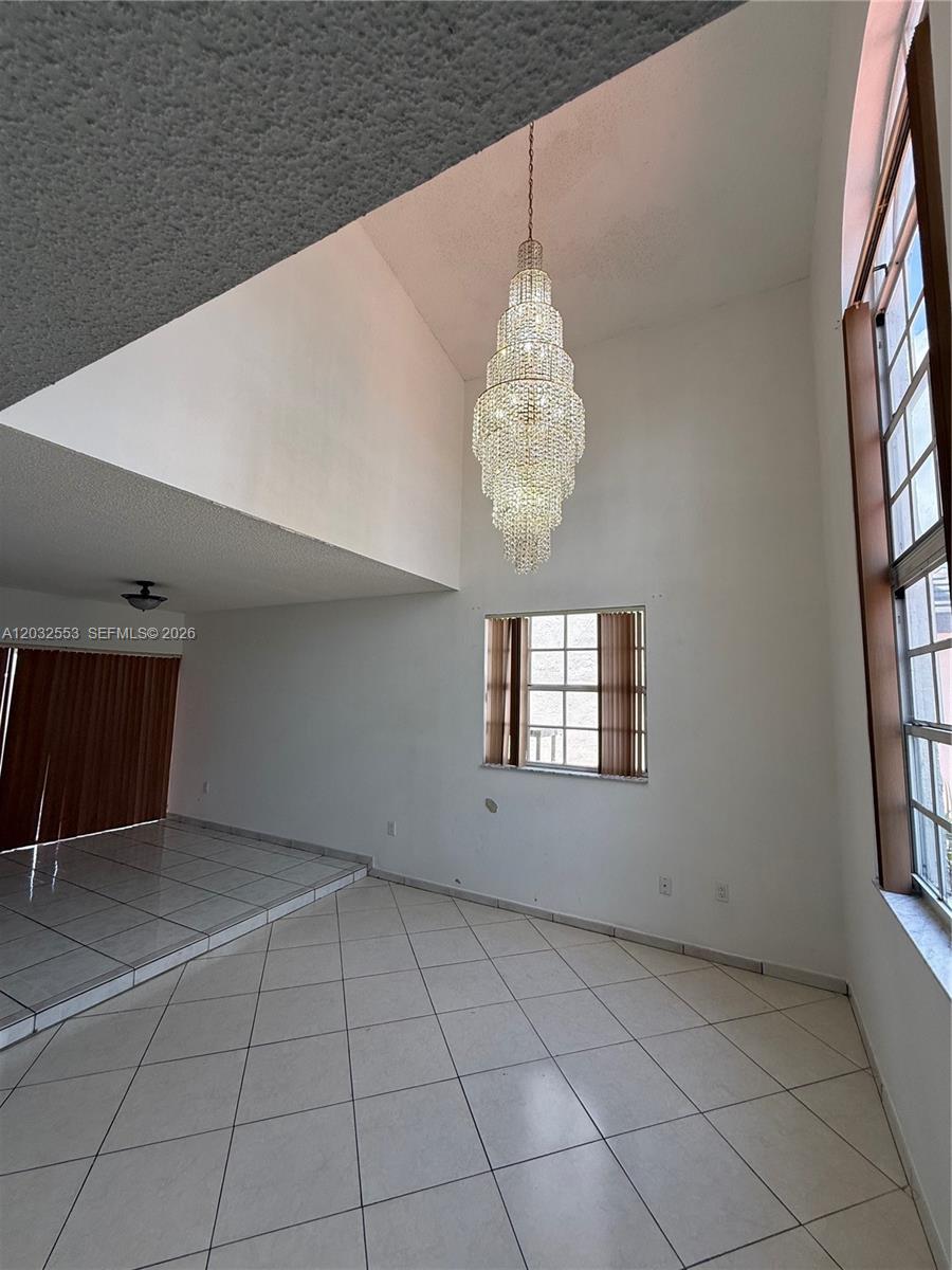 A living room features a high vaulted ceiling, a large crystal chandelier, and tiled floors — 9940 SW 146th Ct, Miami FL 33186, MIAMI, FL