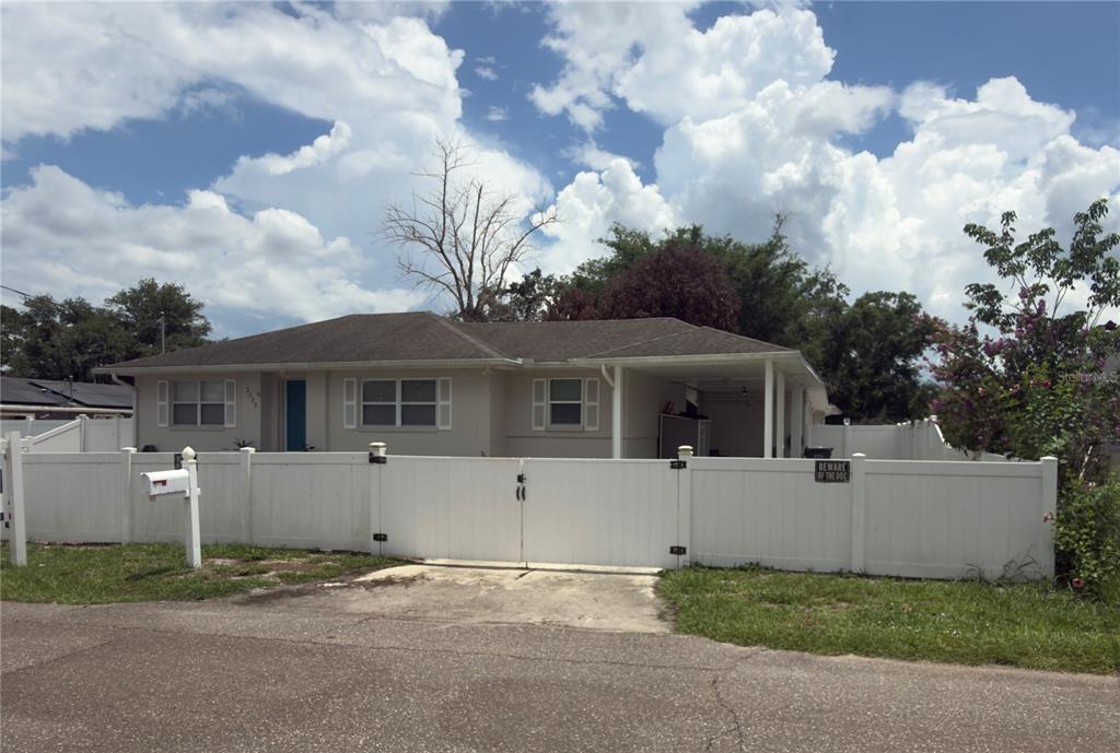 A single-story house with a white vinyl fence and a carport under a cloudy sky — 2523 WEBER STREET, LAKELAND, FL