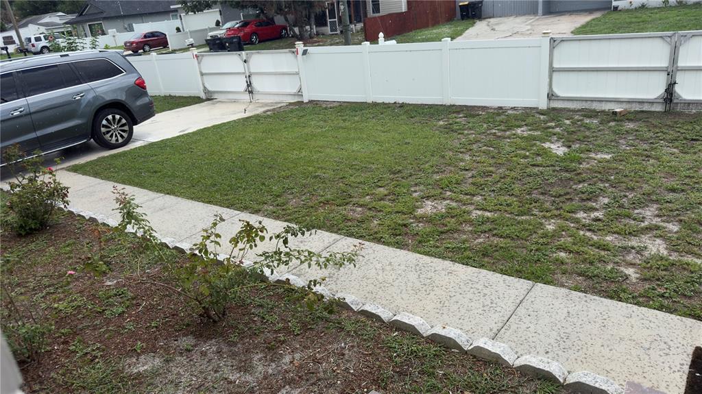 A view of a residential front yard with a concrete walkway, lawn, and white fence — 2523 WEBER STREET, LAKELAND, FL