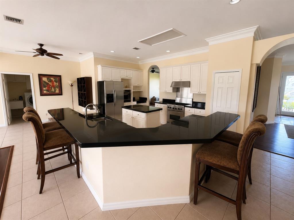 A kitchen features white cabinetry, black countertops, a central island, and two bar stools — 13644 DORNOCH DRIVE, ORLANDO, FL