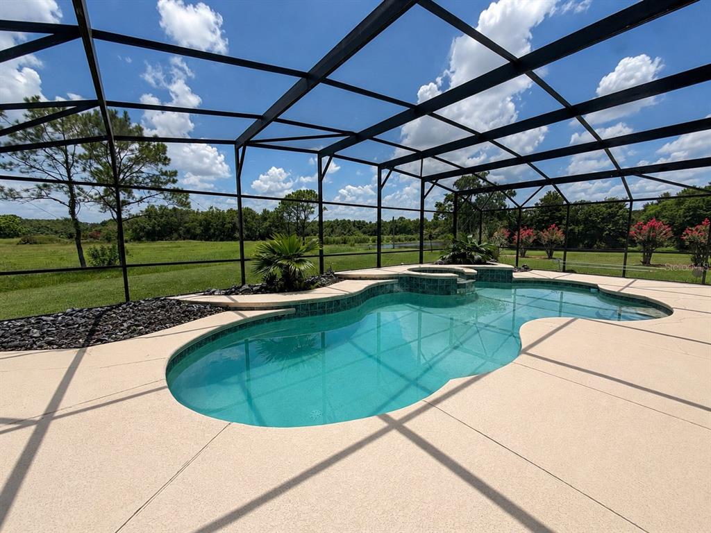 A swimming pool with an attached spa is enclosed by a screened lanai overlooking grass — 13644 DORNOCH DRIVE, ORLANDO, FL