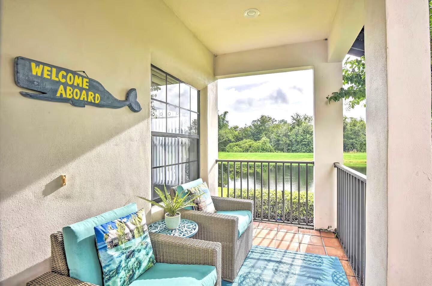 A covered balcony features two wicker chairs, a small table, and a view of a pond — 16708 Lazy Breeze Loop # 16708, Clermont FL 34714, CLERMONT, FL