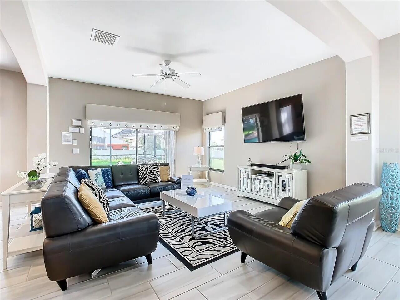 A living room features a black leather sectional, a zebra-print rug, and a wall-mounted television — 16708 Lazy Breeze Loop # 16708, Clermont FL 34714, CLERMONT, FL