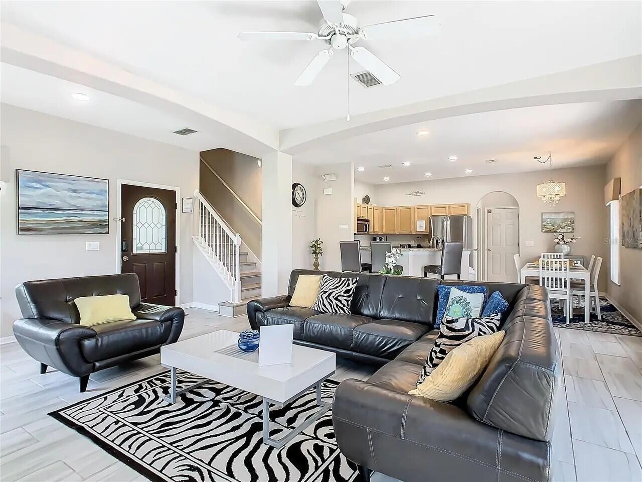 An open-concept living room features a dark leather sectional, zebra-print rug, and adjacent kitchen area — 16708 Lazy Breeze Loop # 16708, Clermont FL 34714, CLERMONT, FL