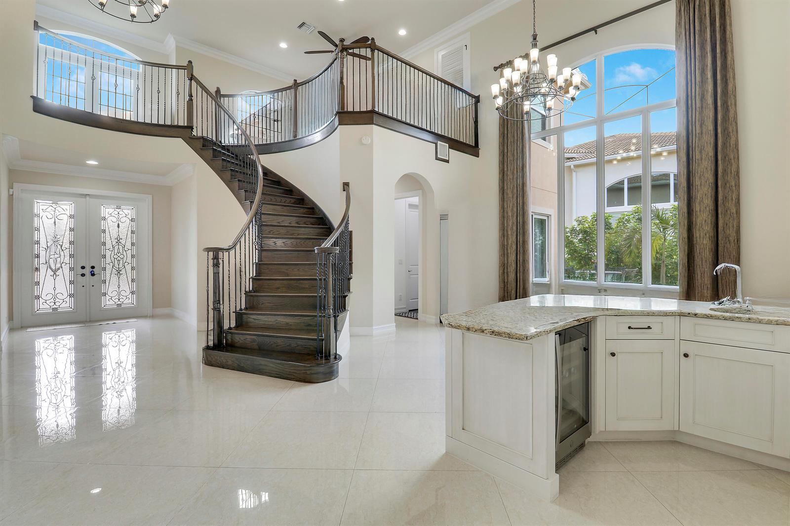 A grand foyer features a curved wooden staircase, tile flooring, and a wet bar area — 167 Rosalia Court S, Jupiter FL 33478, JUPITER, FL