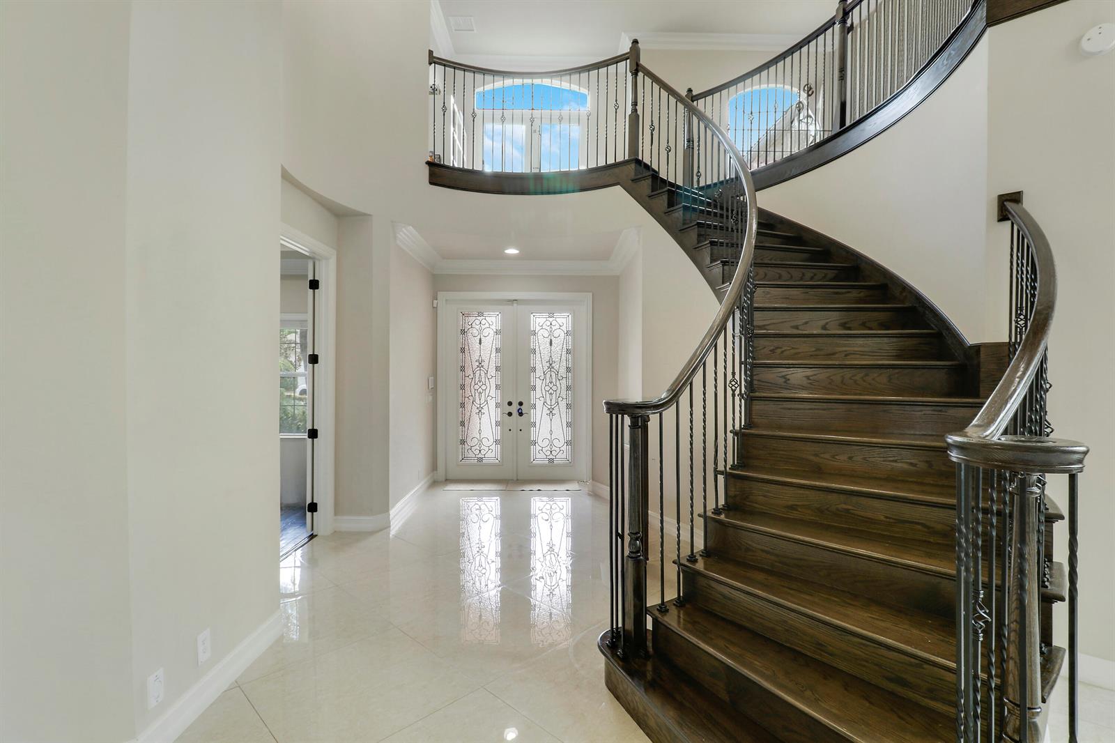 A grand foyer features a curved wooden staircase with iron railings and double glass doors — 167 Rosalia Court S, Jupiter FL 33478, JUPITER, FL