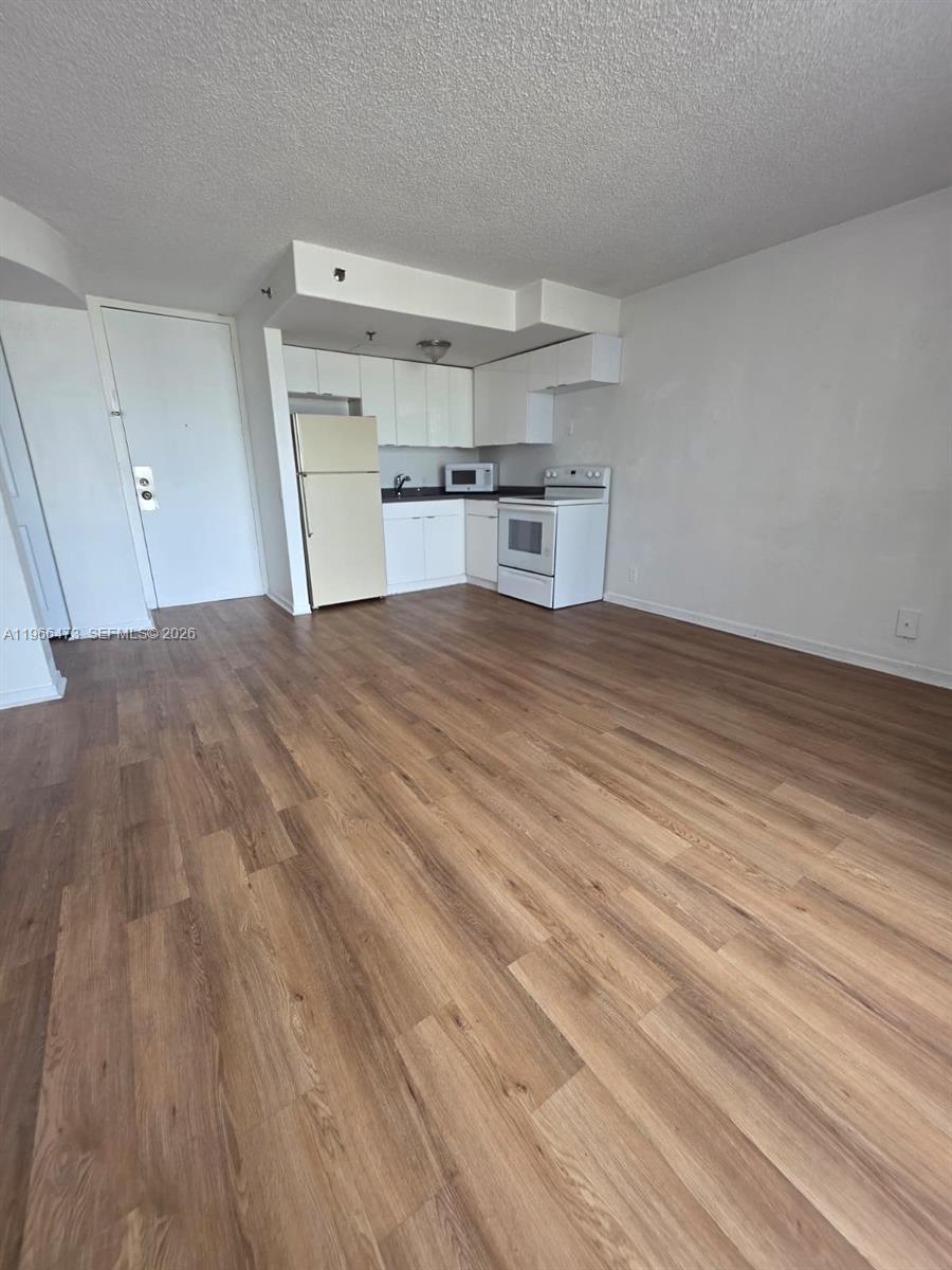 This room features a small kitchen with white cabinets, appliances, and light wood-look flooring — 16450 NW 2nd Ave # 214, Miami FL 33169, MIAMI, FL