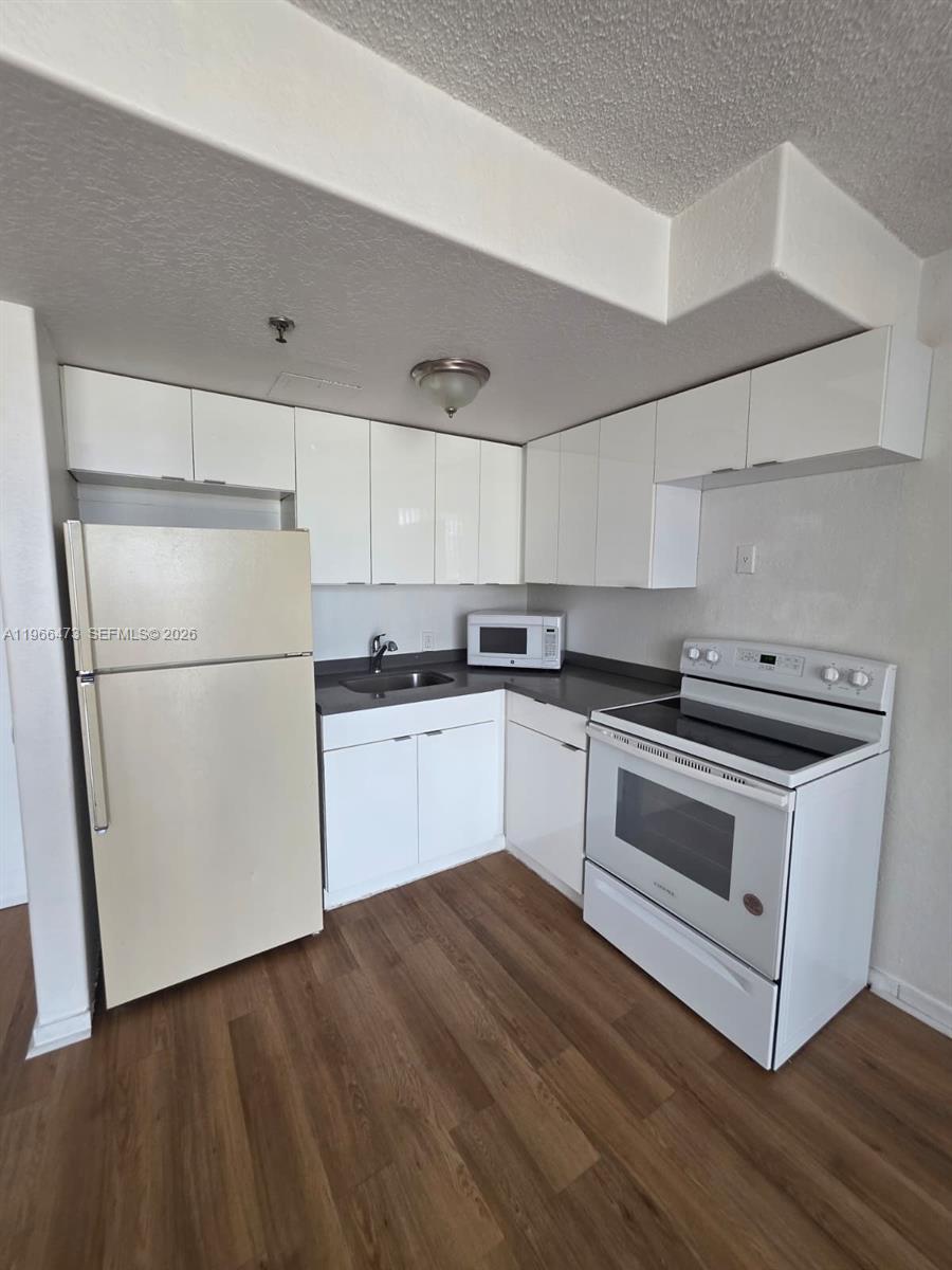 A kitchen features white cabinets, a refrigerator, a stove, and wood-look flooring — 16450 NW 2nd Ave # 214, Miami FL 33169, MIAMI, FL
