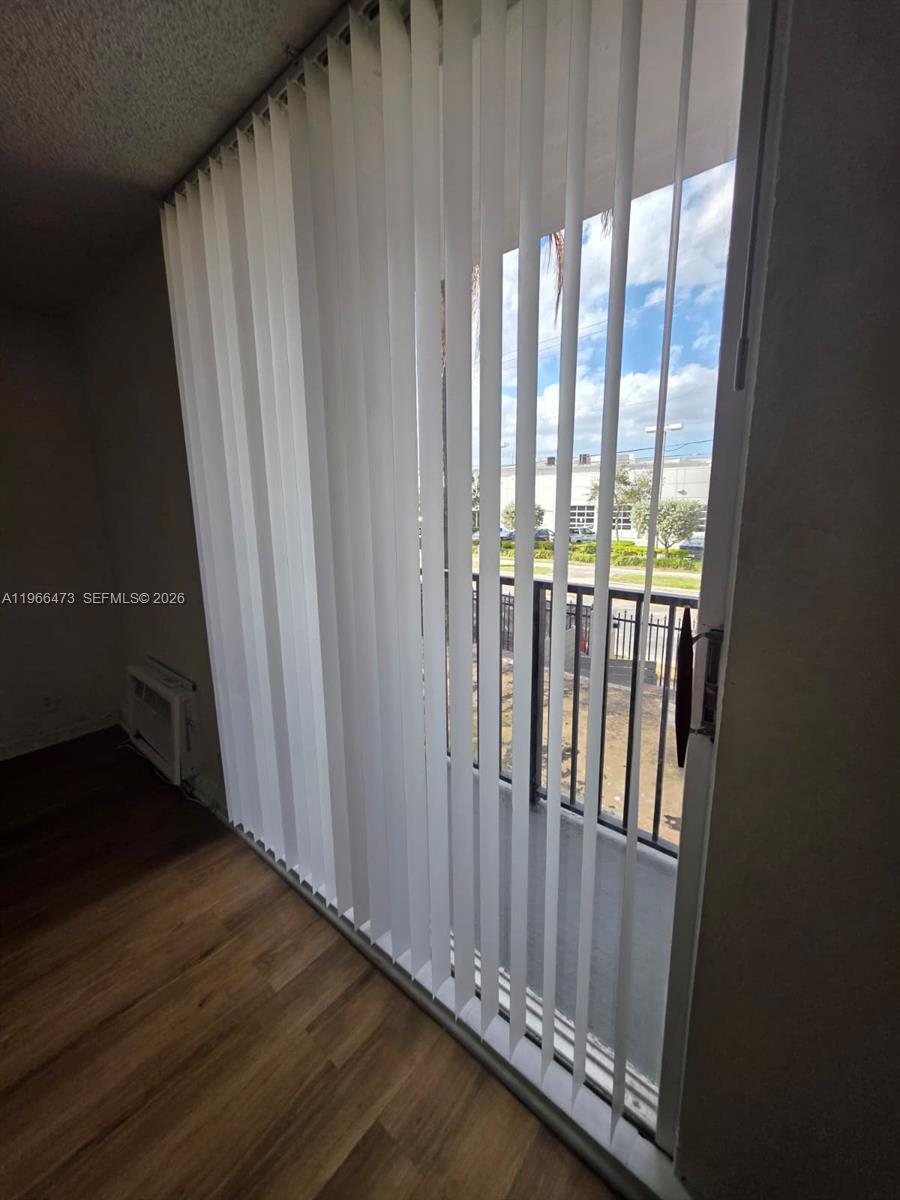 A room with wood-look flooring features a sliding glass door covered by vertical blinds — 16450 NW 2nd Ave # 214, Miami FL 33169, MIAMI, FL
