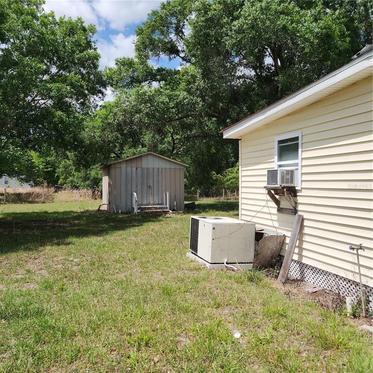 A yellow house exterior features a window air conditioner, a ground-level HVAC unit, and a shed — 26739 FOAMFLOWER BOULEVARD, WESLEY CHAPEL, FL