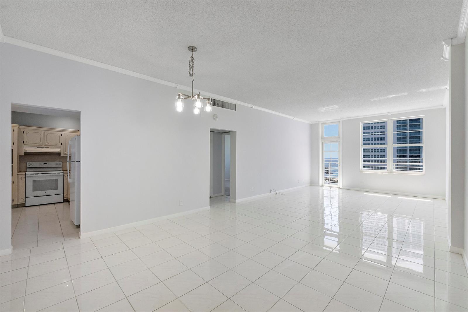 A bright, empty living room with white tile floors, a chandelier, and a kitchen view — 2851 S Ocean Boulevard, Boca Raton FL 33432, BOCA RATON, FL