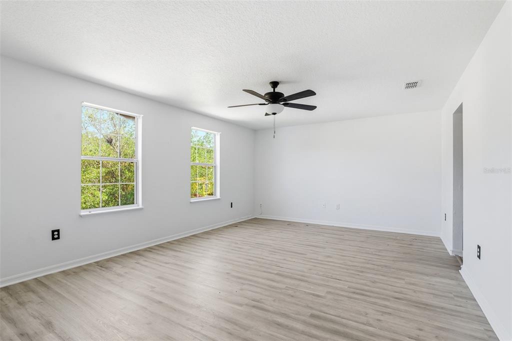 An empty room with white walls, light wood-look flooring, two windows, and a ceiling fan — 3356 SLATE STREET, WEST MELBOURNE, FL