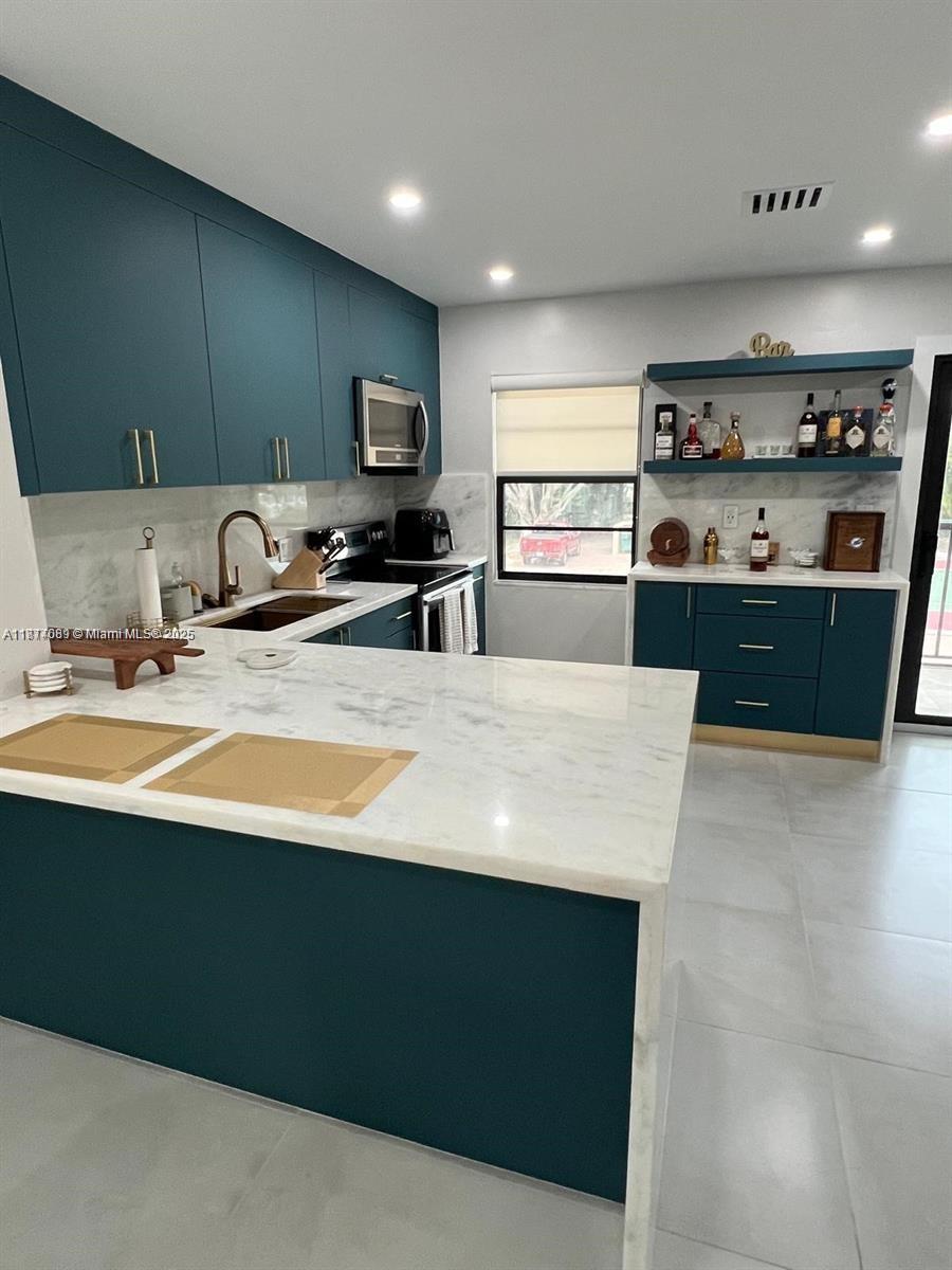A modern kitchen features teal cabinets, a white marble island, and a built-in bar area — 1103 S collier # 108, Marco Island FL 34145, MARCO ISLAND, FL