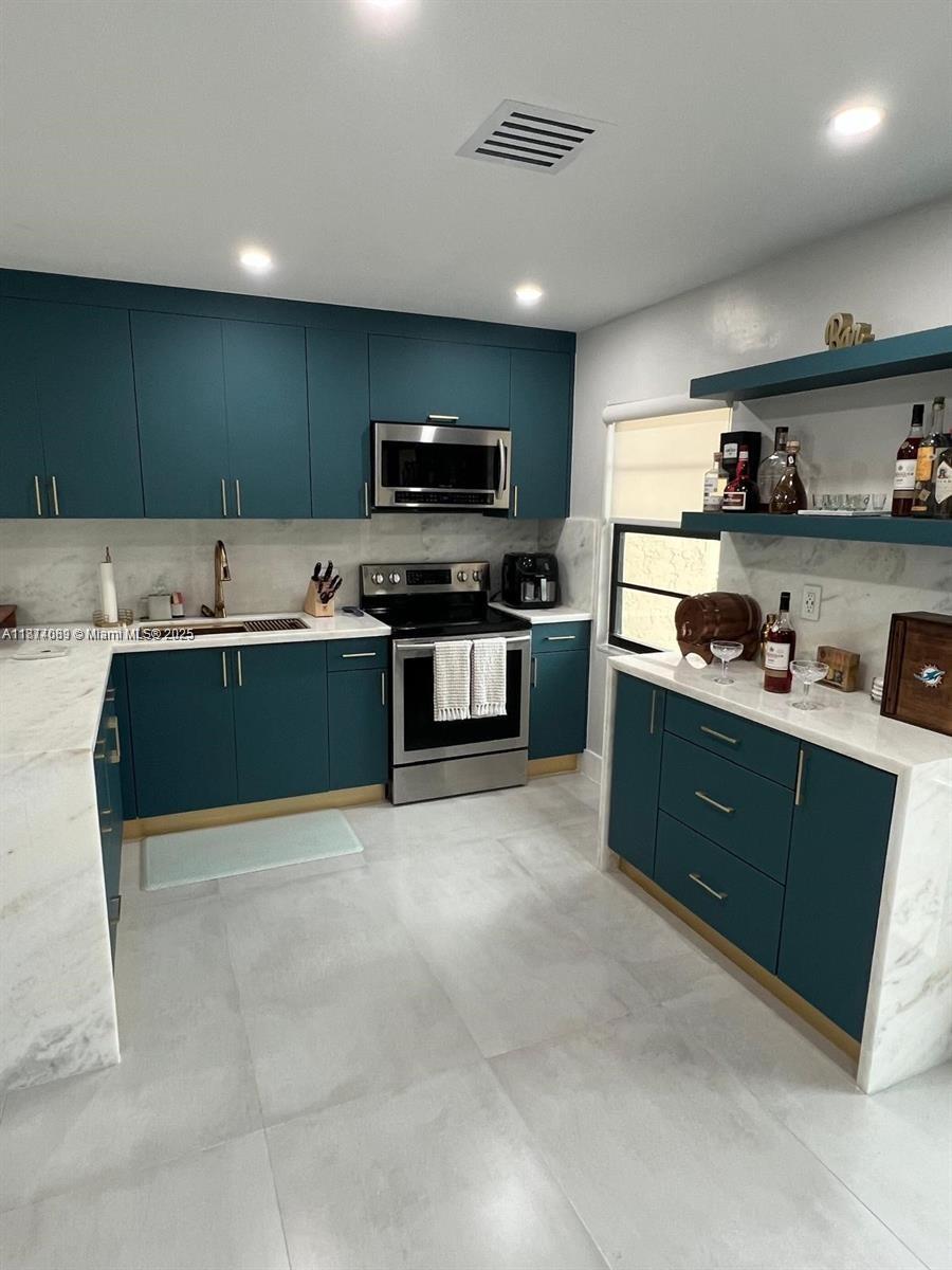 A modern kitchen features teal cabinets, white marble countertops, and stainless steel appliances — 1103 S collier # 108, Marco Island FL 34145, MARCO ISLAND, FL