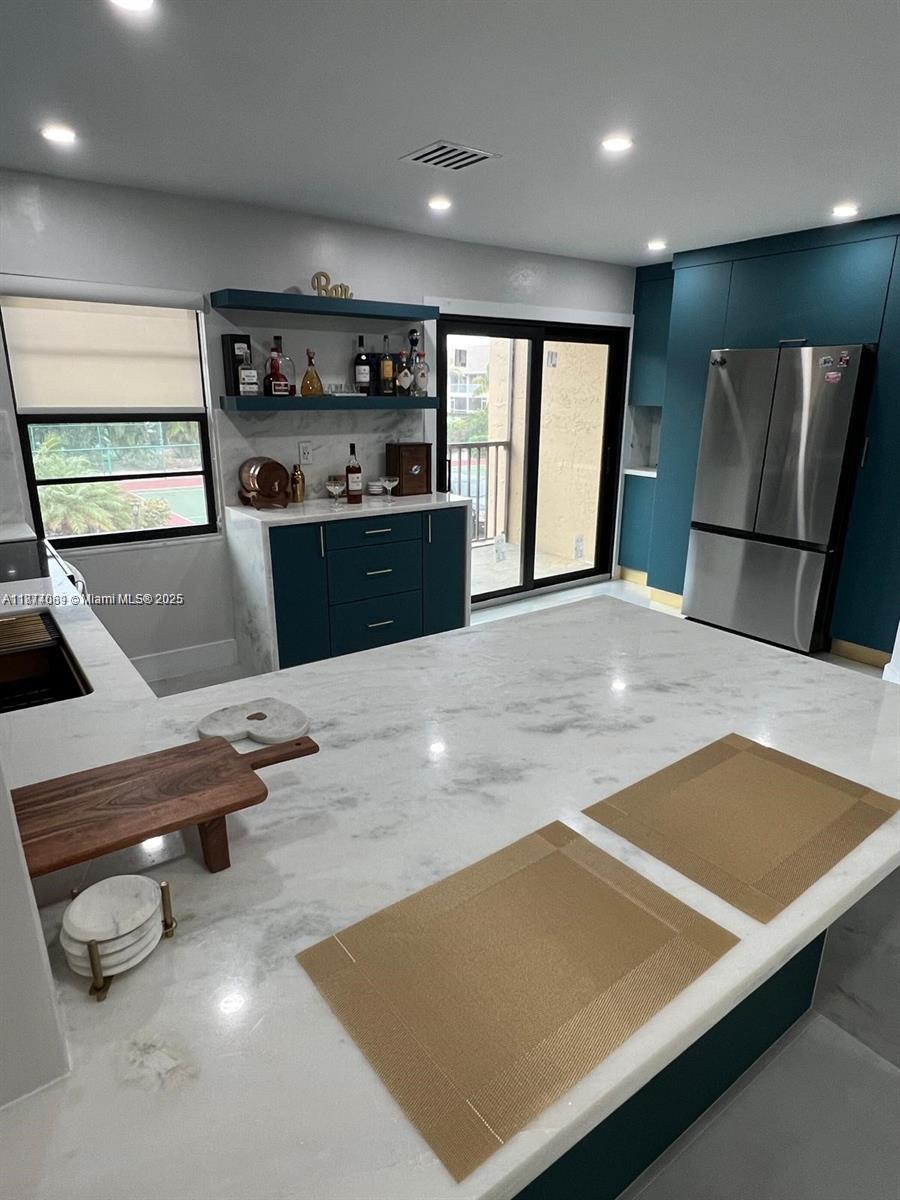 A kitchen features a large marble island, teal cabinetry, a built-in bar, and stainless steel appliances — 1103 S collier # 108, Marco Island FL 34145, MARCO ISLAND, FL
