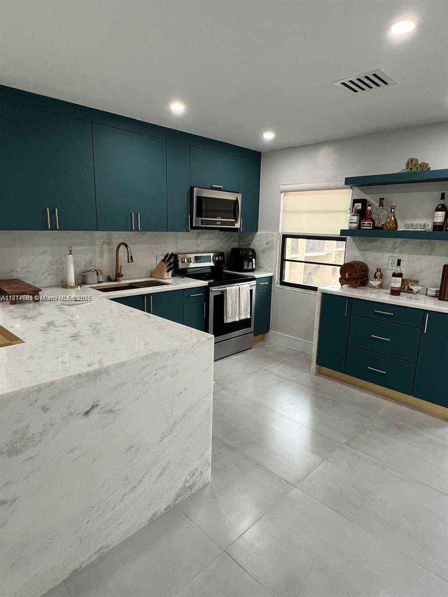 A modern kitchen features teal cabinets, white marble countertops, and light gray floor tiles — 1103 S collier # 108, Marco Island FL 34145, MARCO ISLAND, FL