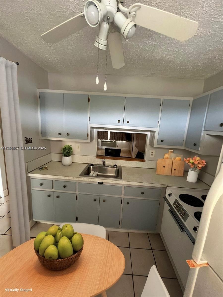 A small kitchen features light blue cabinets, a stainless steel sink, and a ceiling fan — 4299 NW 16th St # 307, Lauderhill FL 33313, LAUDERHILL, FL