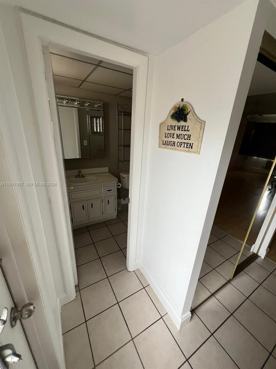A tiled hallway leads to a bathroom with a white vanity and a wall sign — 4299 NW 16th St # 307, Lauderhill FL 33313, LAUDERHILL, FL