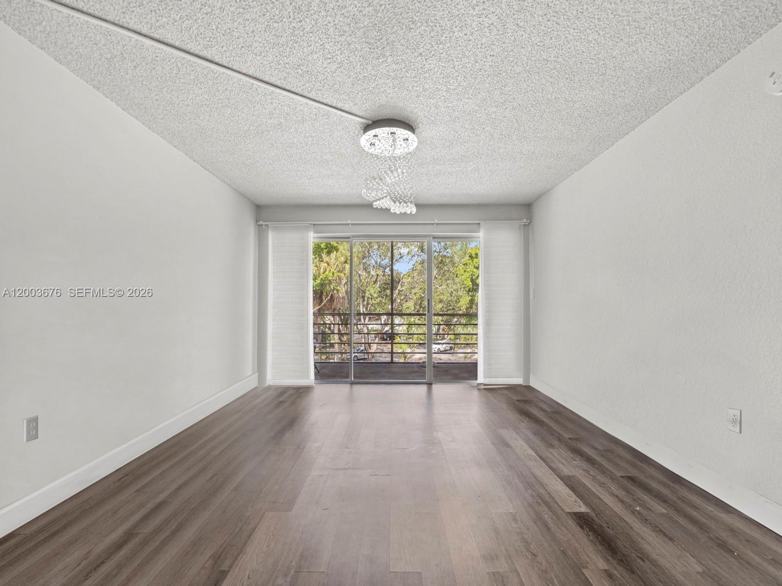 An empty room features wood-look flooring, white walls, a textured ceiling, and a sliding glass door — 4235 N University Dr # 312, Sunrise FL 33351, SUNRISE, FL