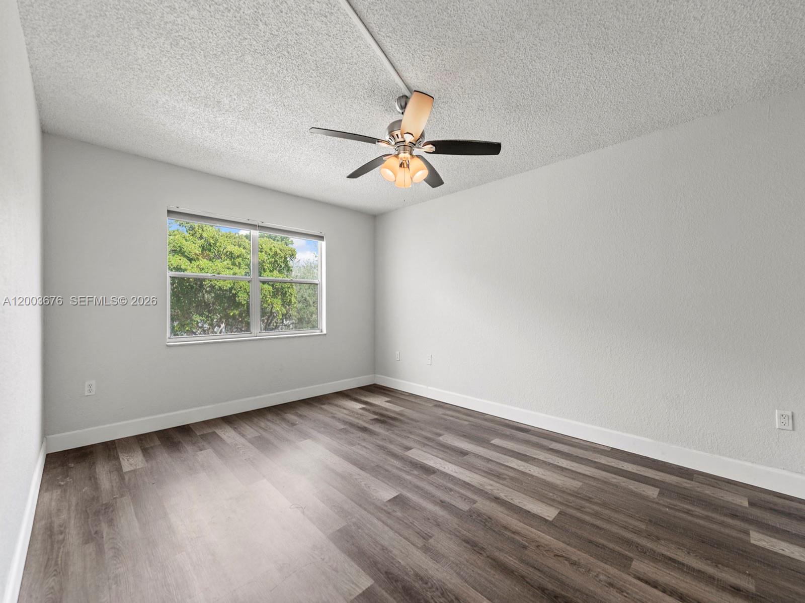 An empty bedroom features light gray walls, wood-look flooring, a ceiling fan, and a window — 4235 N University Dr # 312, Sunrise FL 33351, SUNRISE, FL