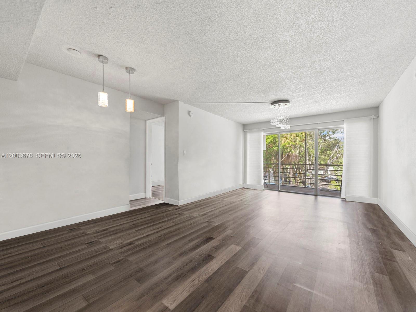 An empty living room features wood-look flooring, a textured ceiling, pendant lighting, and sliding glass doors — 4235 N University Dr # 312, Sunrise FL 33351, SUNRISE, FL