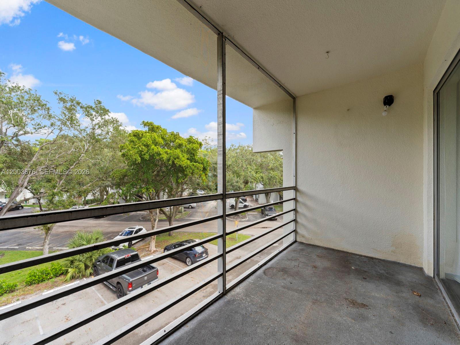 A balcony with a metal railing overlooks a parking lot and trees — 4235 N University Dr # 312, Sunrise FL 33351, SUNRISE, FL