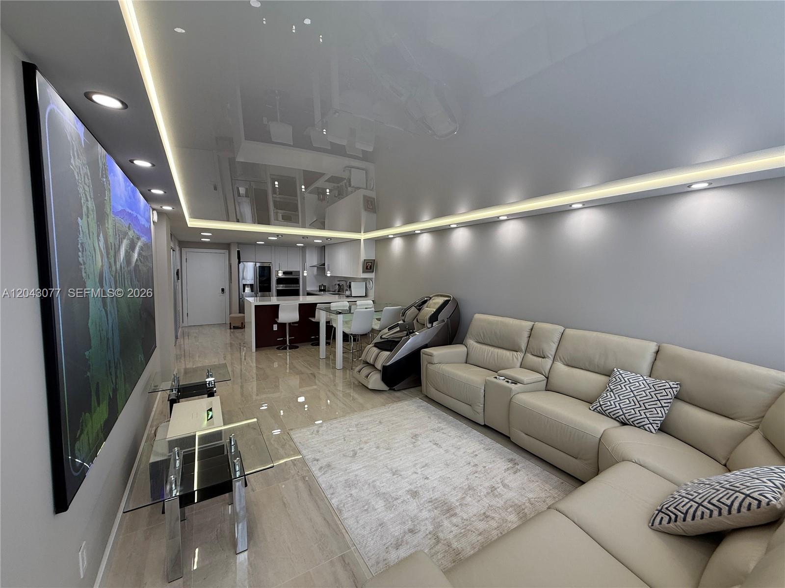 A modern living room features a glossy ceiling, recessed lighting, and a large wall-mounted screen — 1849 S Ocean Dr, Hallandale Beach FL 33009, HALLANDALE BEACH, FL