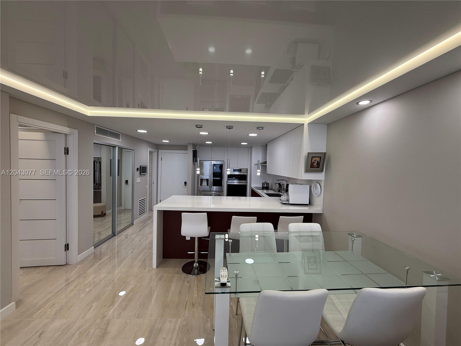 A modern kitchen features a white island, glossy ceiling, and glass dining table — 1849 S Ocean Dr, Hallandale Beach FL 33009, HALLANDALE BEACH, FL