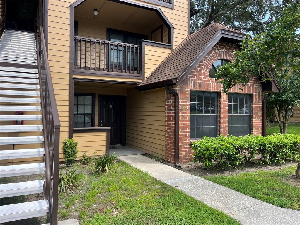 A two-story apartment building exterior features tan siding, a brick facade, and an outdoor staircase — 315 LAKEPOINTE DRIVE UNIT 102, ALTAMONTE SPRINGS, FL