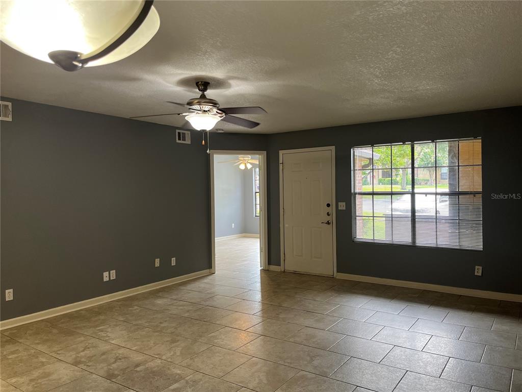 A living room with gray walls, tile flooring, a ceiling fan, and a front door — 315 LAKEPOINTE DRIVE UNIT 102, ALTAMONTE SPRINGS, FL