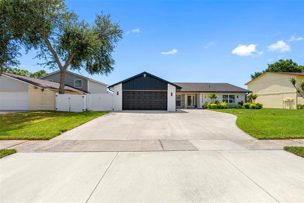 A single-story house with a black garage door and a concrete driveway under a blue sky — 16206 W COURSE DRIVE, TAMPA, FL