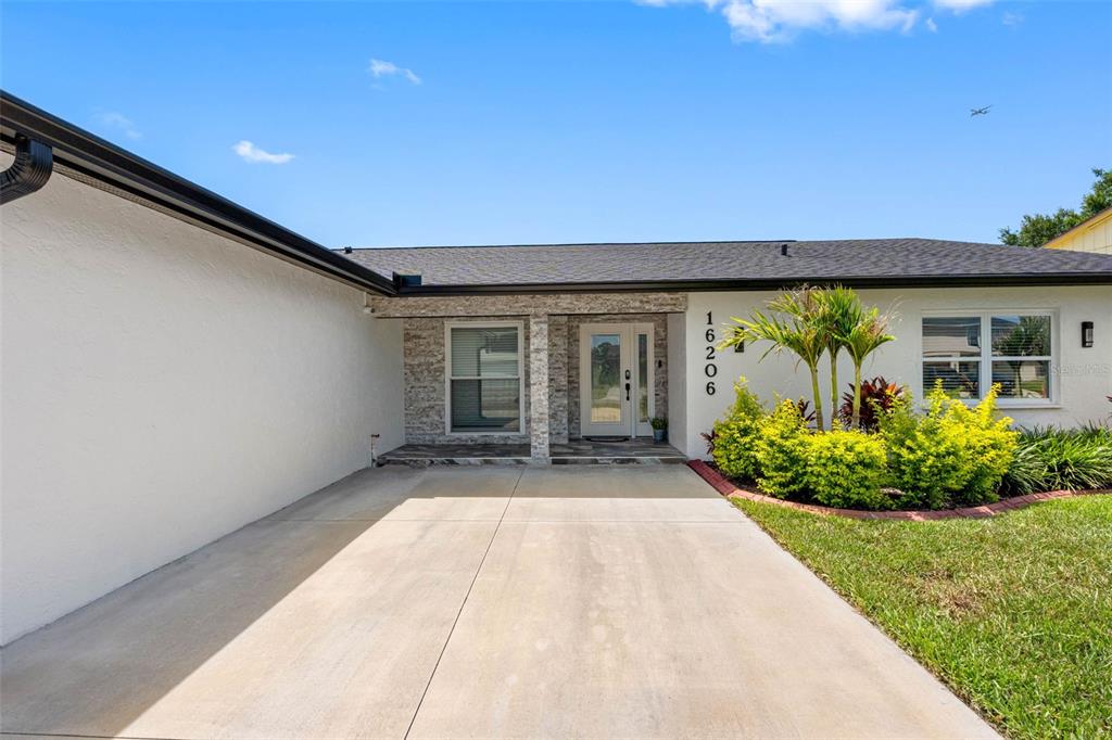 The exterior of a single-story house features a concrete driveway, stone accents, and landscaping — 16206 W COURSE DRIVE, TAMPA, FL