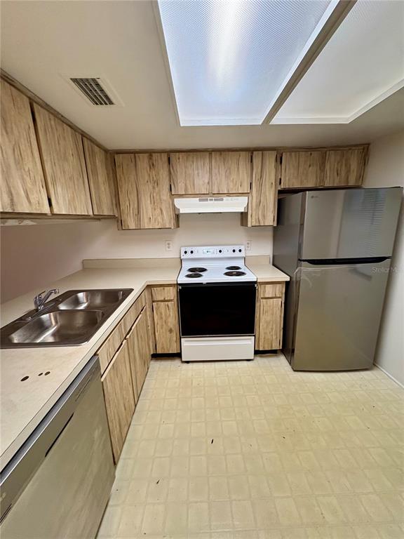 A kitchen features wood-grain cabinets, a stainless steel refrigerator, a white stove, and linoleum flooring — 5038 TERRACE PALMS CIRCLE UNIT 202, TAMPA, FL