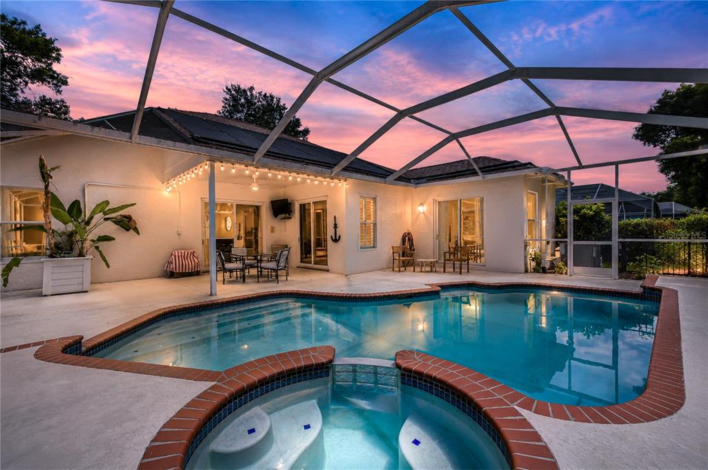 A screened-in patio features a swimming pool, a hot tub, and string lights at sunset — 3530 FOX SQUIRREL LANE, VALRICO, FL