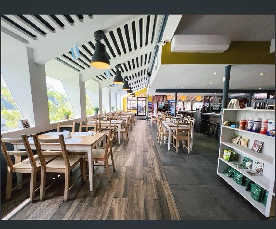 A restaurant interior features wooden tables, chairs, pendant lighting, and a retail display shelf — Punta Las Marias 33 & 35 CAOBA, SAN JUAN, PR