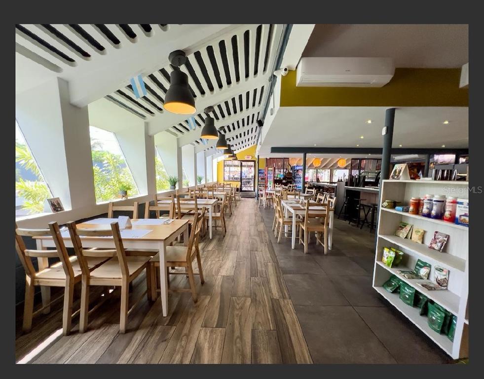 A restaurant interior features wooden tables, chairs, pendant lighting, and a retail display shelf — Punta Las Marias 33 & 35 CAOBA, SAN JUAN, PR
