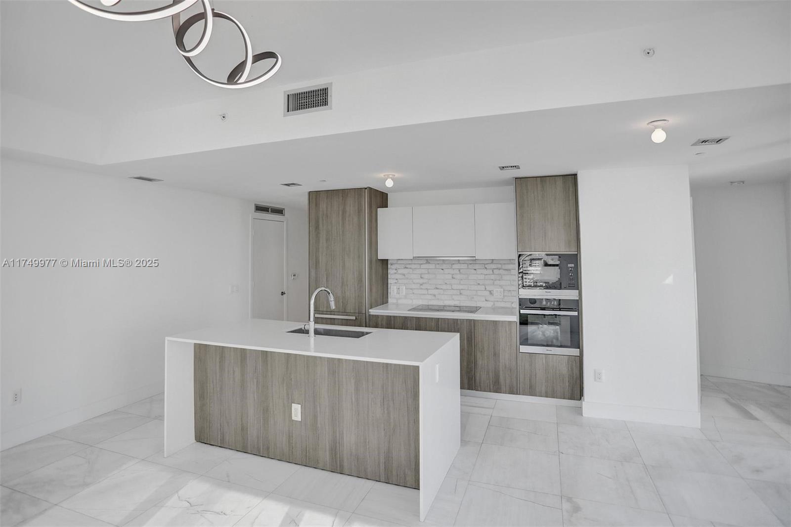 A modern kitchen features a white island, wood-grain cabinetry, and a white brick backsplash — 2900 NE 7th Ave # 1601, Miami FL 33137, MIAMI, FL
